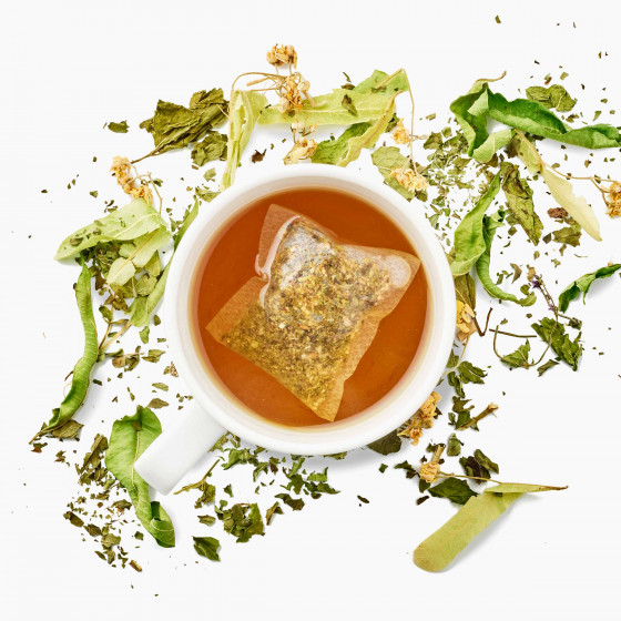 tasse d'infusion à la menthe, au tilleul et à la verveine avec le sachet dans la tasse et les plantes séchées autour